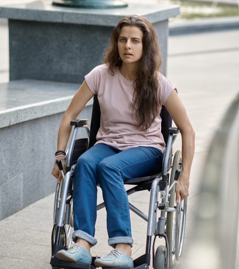 Disabled woman in wheelchair climbs the ramp. Paralyzed people and disability, handicap overcoming. Handicapped female person walking in park