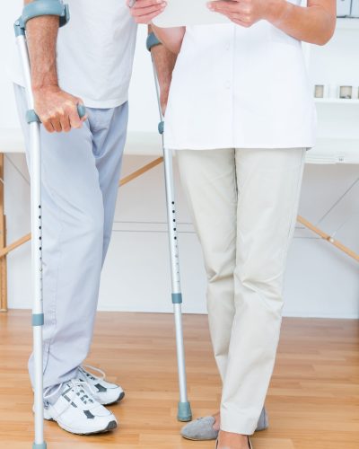 Doctor showing clipboard to her patient with crutch in medical office